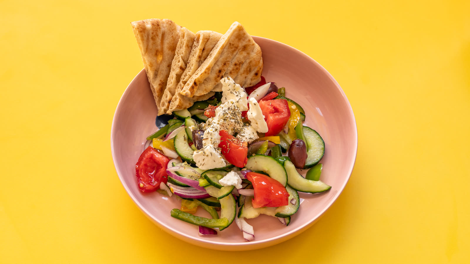 Greek salad in a pink bowl, with triangles of pita