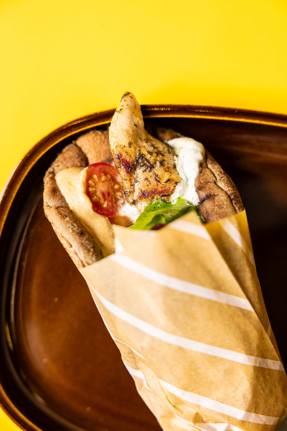 Chicken souvlaki wrap in a wholemeal pita with tzatziki, tomato and salad, in its striped paper