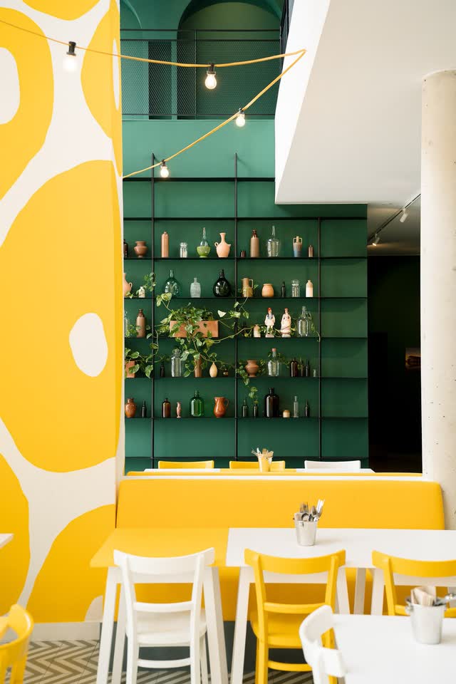 Inside KALIMERA Bordeaux: yellow chairs, a yellow and white mural and green shelves lined with jars and bottles