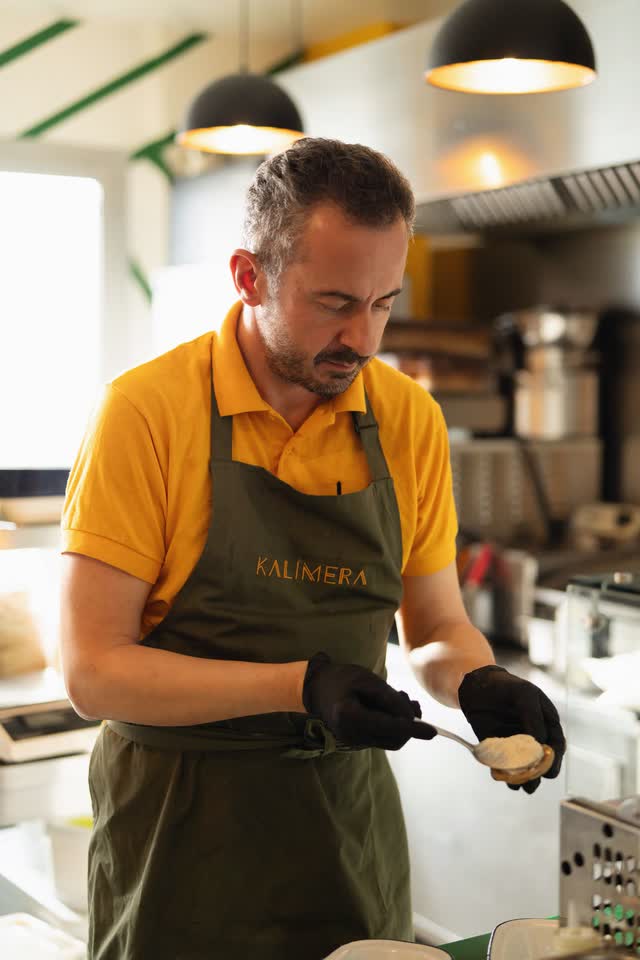 A KALIMERA cook in a yellow polo and olive apron at work in the kitchen at Ground Control