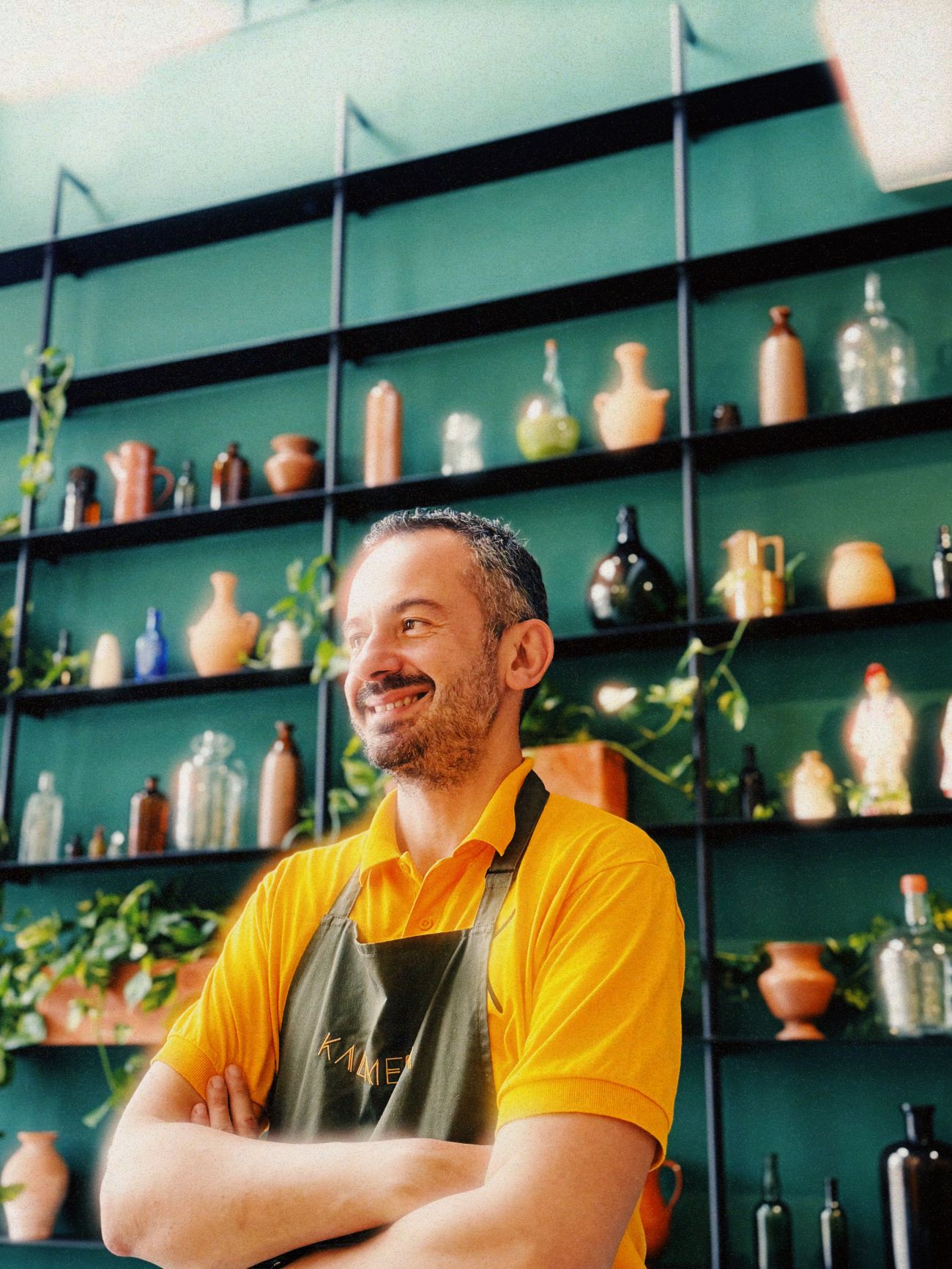 Télémaque Argyriou, founder of KALIMERA, arms folded, in a yellow polo and olive apron