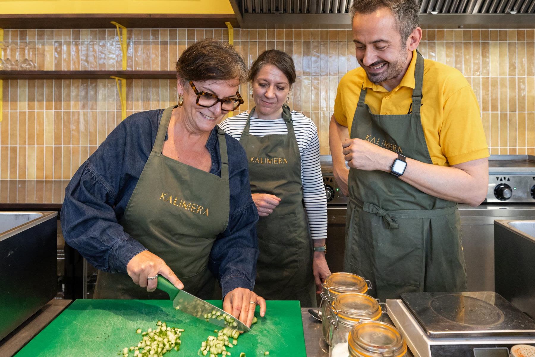 A KALIMERA cooking workshop in Bordeaux: a guest dices cucumber at the kitchen counter while another guest and their host look on, laughing