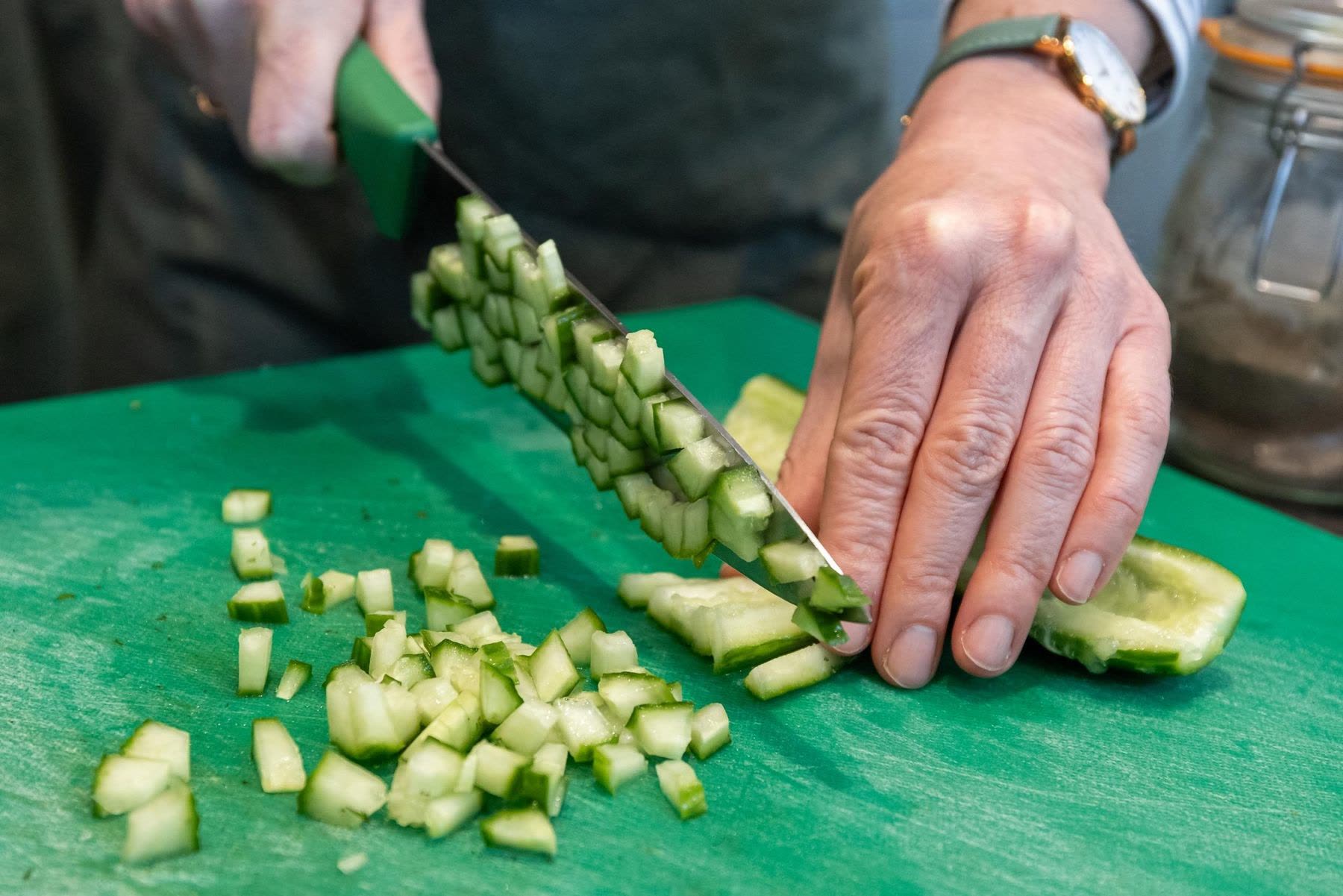 Hands dicing cucumber on a green board during a KALIMERA cooking workshop